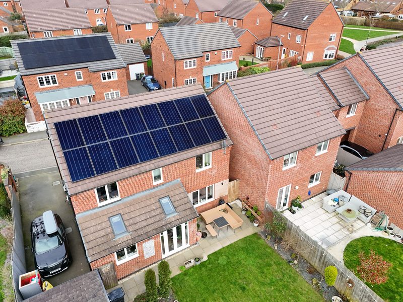 Aerial view of a red-brick new-build home with a dark solar panel array on the front roof pitch