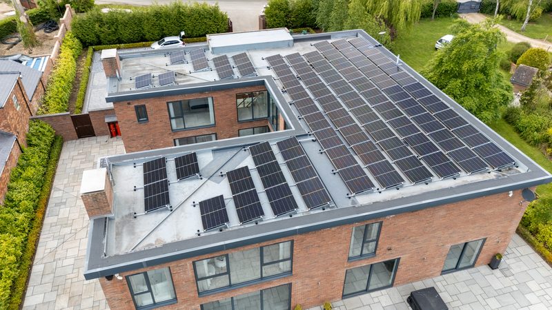 Aerial view of a large flat-roof solar array of around ninety panels on a modern brick home