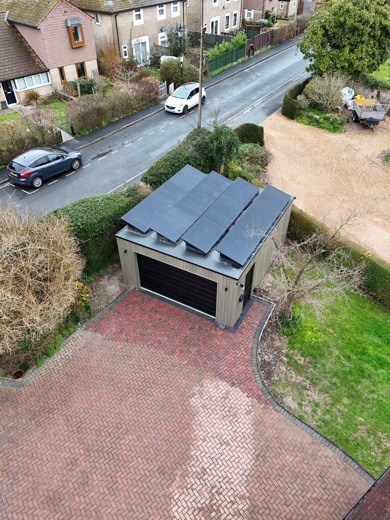 Aerial view of a flat-roof garden building with a black solar panel array, on a residential street