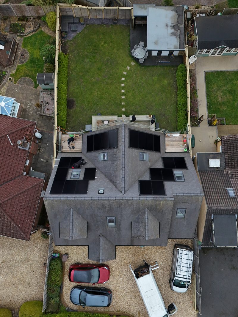 Aerial view of solar panels being fitted across several roof dormers on a grey-rendered home