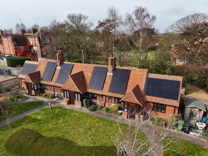 Aerial view of a row of red-brick heritage cottages with solar panels spaced along the roof ridge