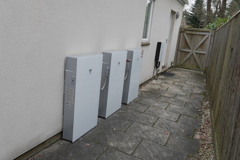 Three Tesla Powerwall battery units mounted side by side on a rendered exterior wall