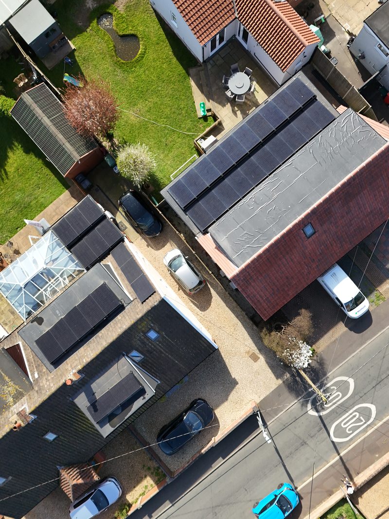 Aerial view of a residential UK street where several homes have black solar panels fitted to rear roof pitches