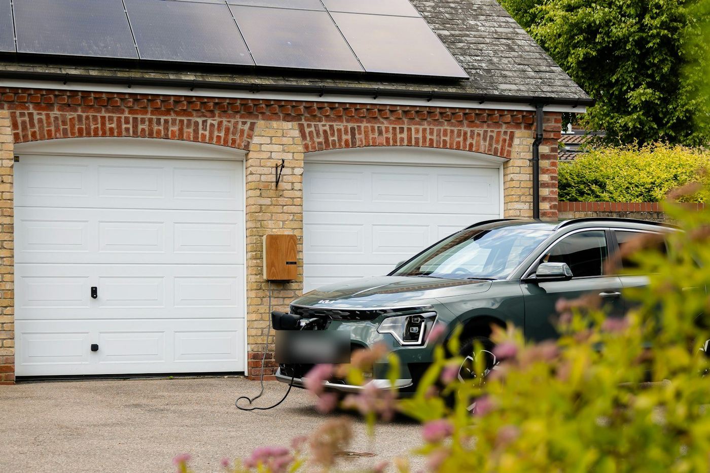 An electric car charging outside a brick garage with solar panels above